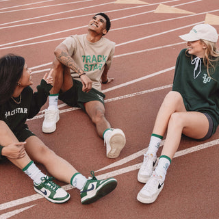Two woman and one man sitting on a track wearing Track Star socks and other Life360 merchandise